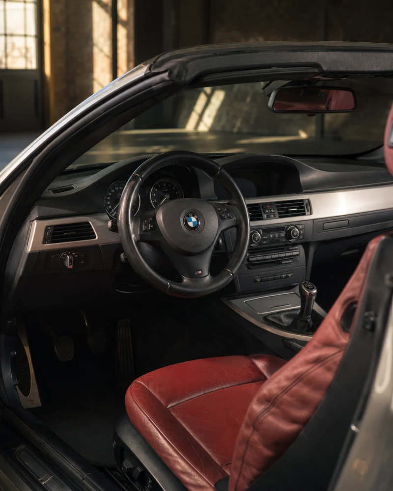 Interior BMW din anii 2000, cu instrumente analogice, butoane fizice și piele roșie – imagine ilustrativă generată cu inteligență artificială.